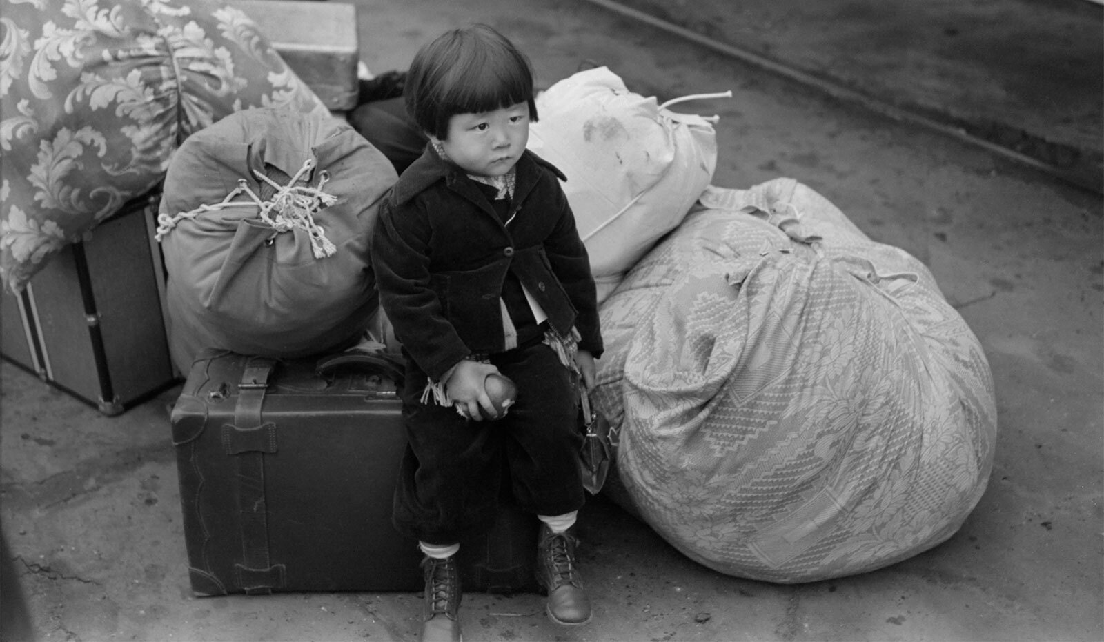 This image shows a 1942 photograph of a Japanese-American child waiting for train in Los Angeles, California.