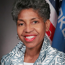 This image depicts a headshot of Oklahoma State Representative and Chair of the Oklahoma Legislative Black Caucus, Regina Goodwin, in front of the flags of the United States of America and the State of Oklahoma.